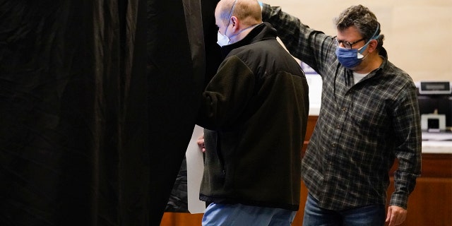 An election worker helps a voter into a booth at a polling place at the Museum of the American Revolution in Philadelphia, Nov. 2, 2021.