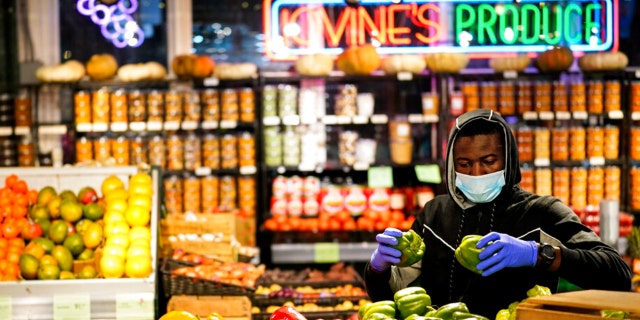 A grocer wearing a protective mask as a precaution against the spread of the coronavirus stocks papers at the Reading Terminal Market in Philadelphia, Wednesday, Feb. 16, 2022.
