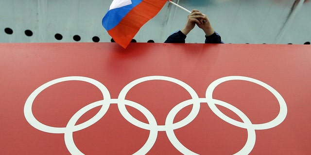 FILE - A Russian flag is held above the Olympic Rings at Adler Arena Skating Center during the Winter Olympics in Sochi, Russia on Feb. 18, 2014. The International Olympic Committee has made a sweeping move to isolate and condemn Russia over the country’s invasion of Ukraine.