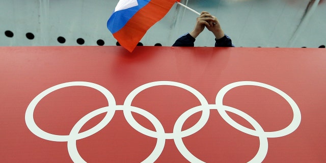 FILE - A Russian flag is held above the Olympic Rings at Adler Arena Skating Center during the Winter Olympics in Sochi, Russia on Feb. 18, 2014. The International Olympic Committee has made a sweeping move to isolate and condemn Russia over the country’s invasion of Ukraine.