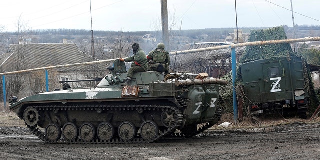Service members of pro-Russian troops in uniforms without insignia driving an armored vehicle with the symbol 