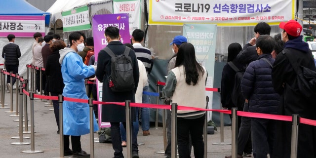 A medical worker guides people waiting for a coronavirus test at a makeshift testing site in Seoul, South Korea, Thursday, March 17, 2022.