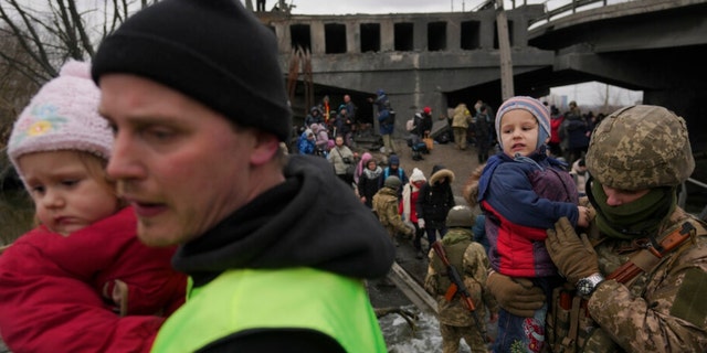 Um soldado ucraniano segura um bebê atravessando o rio Irpin em um caminho improvisado sob uma ponte que foi destruída por um ataque aéreo russo, enquanto ajudava pessoas que fugiam da cidade de Irpin, na Ucrânia, no sábado, 5 de março de 2022. 