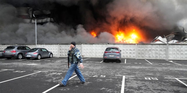 A Ukrainian serviceman walks past as fire and smoke rises over a damaged logistic center after shelling in Kyiv, Ukraine, Thursday, March 3, 2022.