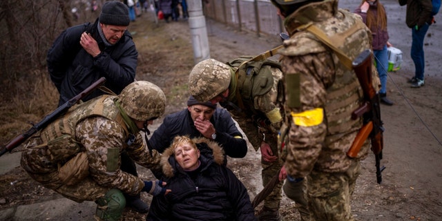 Une femme semi-consciente est prise en charge par des soldats ukrainiens après avoir traversé la rivière Irpin alors qu'elle fuyait la ville de la périphérie de Kiev, en Ukraine, le samedi 5 mars 2022.
