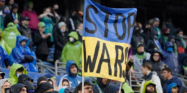 Un supporter des Sounders de Seattle tient une pancarte indiquant "Arrêtez les guerres" lors d'une minute de silence pour les victimes de la guerre en Ukraine, avant le début d'un match de football MLS entre les Sounders et le Nashville SC, dimanche 27 février 2022, à Seattle.