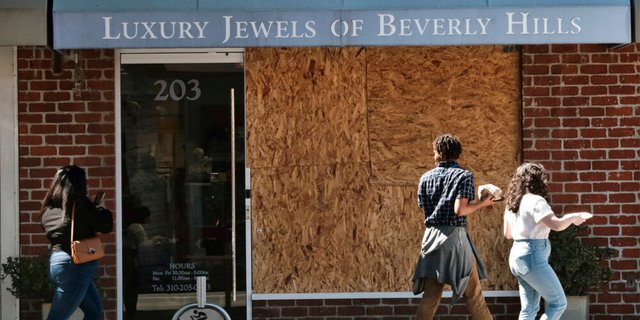 Pedestrians walk past a boarded up Luxury Jewels of Beverly Hills on Wednesday, March 23, 2022 in Beverly Hills, Calif. 