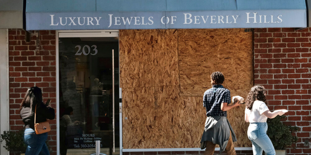 Pedestrians walk past a boarded up Luxury Jewels of Beverly Hills on Wednesday, March 23, 2022 in Beverly Hills, Calif.