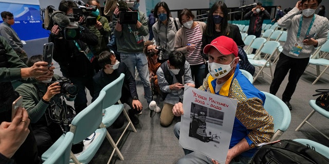 A journalist from Ukraine holding a photo of Yevhen Malyshev, a 19-year-old former athlete on Ukraine's junior biathlon team who, according to the International Biathlon Union, died serving the Ukraine military, is surrounded by other journalists after a press conference at the 2022 Winter Paralympics in Beijing, Wednesday, March 2, 2022.