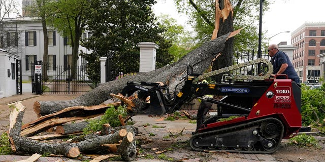 A state grounds engineer uses a mini skid steer to remove some of the limbs and trunk from this downed tree that was felled by strong winds on the grounds of the Mississippi Governor's Mansion onto a main intersection of downtown Jackson, during an outbreak of severe weather in the state, Wednesday, March 30, 2022. A section of the security fence and the decorative brick wall was damaged by the tree. 