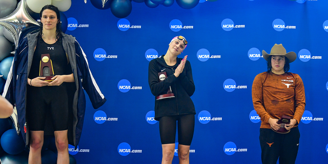 La nadadora de la Universidad de Pensilvania, Lia Thomas, a la izquierda, acepta el trofeo ganador en la final de estilo libre de 500 m mientras Emma Weyant, en segundo lugar, y Erica Sullivan, en tercer lugar, a la derecha, observan durante los campeonatos de natación y el trampolín de la NCAA.