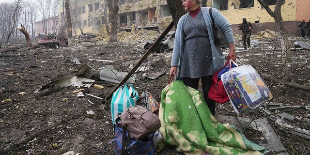 A woman walks outside the damaged by shelling maternity hospital in Mariupol, 乌克兰, 星期三, 游行 9, 2022. A Russian attack has severely damaged a maternity hospital in the besieged port city of Mariupol, Ukrainian officials say.