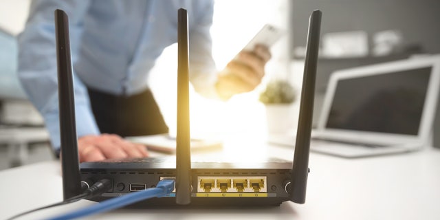 Wireless router with three antennas and cable connected. Man using smartphone in background