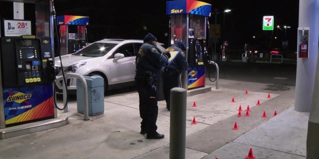 Philadelphia police officers at the scene of a homicide where a man was shot and killed at a gas station. The city has launched a 211 crime prevention hotline to reduce the ongoing violence that continues to plague the city.