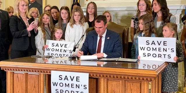 Oklahoma Gov. Kevin Stitt signs a bill in Oklahoma City on Wednesday, March 30, 2022, that prevents transgender girls and women from competing on female sports teams. Stitt signed the bill flanked by more than a dozen young female athletes, including his eighth-grade daughter Piper. (AP Photo/Sean Murphy)