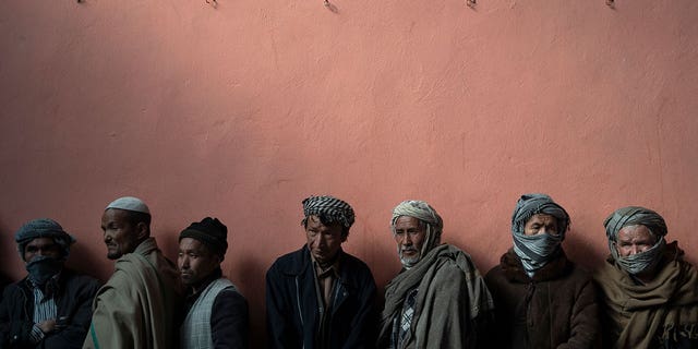 Men wait in a line to receive cash at a money distribution organized by the World Food Program in Kabul, Afghanistan, Nov. 3, 2021.