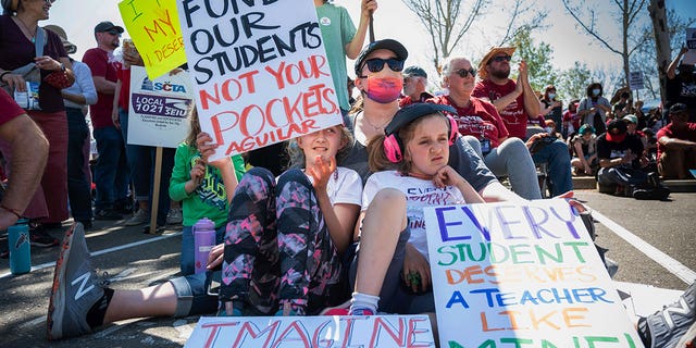 Katie Ragle sits with her daughters Eliana, left, and Delilah, right with headphones, as they support their teachers at Alice Birney Waldorf Inspired K-8 School in front of the Serna Center in Sacramento on Wednesday, March 23, 2022, during the start of the Sacramento City Teachers Association strike.