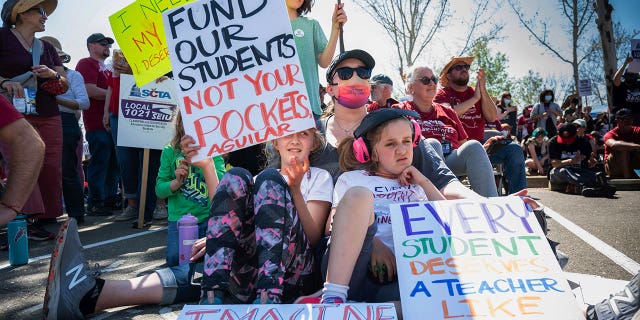 Katie Ragle sits with her daughters Eliana, left, and Delilah, right with headphones, as they support their teachers at Alice Birney Waldorf Inspired K-8 School in front of the Serna Center in Sacramento on Wednesday, March 23, 2022, during the start of the Sacramento City Teachers Association strike.