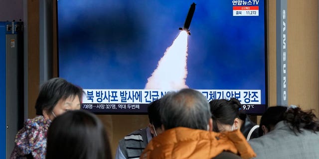 People stand by a TV screen showing a file image of North Korea's rocket launch during a news program, at the Seoul Railway Station in Seoul, South Korea, Sunday, March 20, 2022. (AP Photo/Ahn Young-joon)