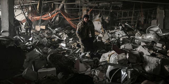 Ukranian servicemen search through rubble inside the Retroville shopping mall after a Russian attack in northwest of Kyiv on March 21, 2022. - At least six people were killed in the overnight bombing of a shopping center in the Ukrainian capital Kyiv, an AFP journalist said, with rescuers combing the wreckage for other victims. The 10-storey building was hit by a powerful blast that pulverized vehicles in its car park and left a crater several meters (yards) wide.