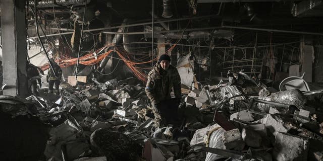 Ukranian servicemen search through rubble inside the Retroville shopping mall after a Russian attack in northwest of Kyiv on March 21, 2022. - At least six people were killed in the overnight bombing of a shopping center in the Ukrainian capital Kyiv, an AFP journalist said, with rescuers combing the wreckage for other victims. The 10-storey building was hit by a powerful blast that pulverized vehicles in its car park and left a crater several meters (yards) wide.