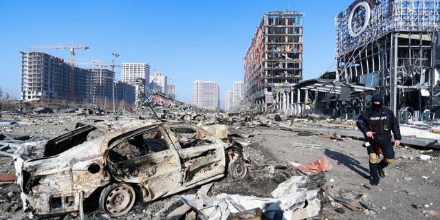 A police officer stands guard next to the Wreckage and debris outside a damaged shopping centre in the Podilskyi district of Kyiv by Russian air strikes, amid Russian invasion, in Kyiv, Ukraine, 21 March 2022. Russian invasions have forced millions of Ukrainians to become refugees fleeing to other countries. (Photo by Ceng Shou Yi/NurPhoto via Getty Images)