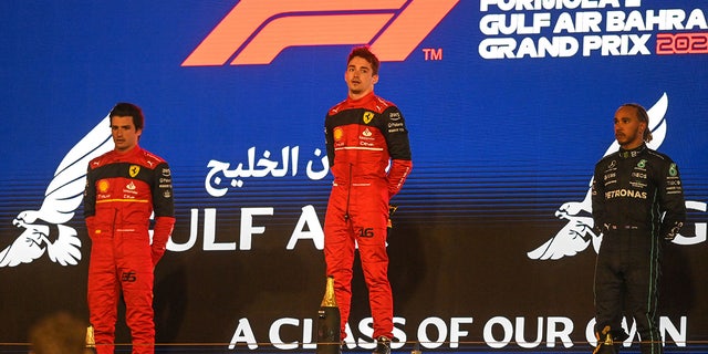 Ferrari's Spanish driver Carlos Sainz Jr (L), Ferrari's Monegasque driver Charles Leclerc (C) and Mercedes' British driver Lewis Hamilton stand for the national anthem on the podium after the Bahrain Formula One Grand Prix at the Bahrain International Circuit in the city of Sakhir on March 20, 2022. (Photo by OZAN KOSE / AFP) (Photo by OZAN KOSE/AFP via Getty Images)