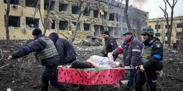 Des employés d'urgence et des volontaires ukrainiens transportent une femme enceinte blessée de la maternité endommagée par les bombardements de Marioupol, en Ukraine, 