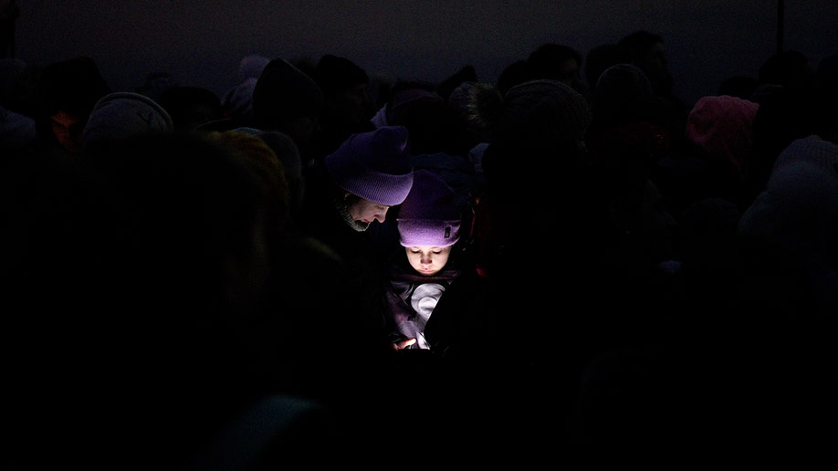 The faces of refugees fleeing the war in Ukraine are illuminated by the light from a smartphone as they join a line approaching the border with Poland in Shehyni, Ukraine, Sunday, March 6, 2022. (AP Photo/Daniel Cole)