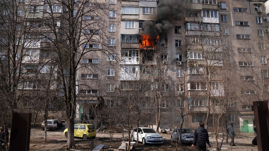 People look at a burning apartment building in a yard after shelling in Mariupol, Ukraine, Sunday, March 13, 2022. (AP Photo/Evgeniy Maloletka)