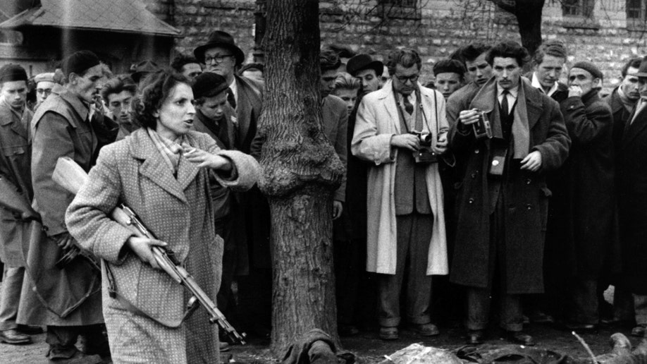 The body of a member of the Hungarian secret police lies in a Budapest street as western journalists witness the anti-communist uprising in Hungary. Even teenagers and women took arms against the communist state, summarily executing those suspected of involvement with the state's secret police (AVH or AVO). Amongst the crowd with his camera is photographer John Sadhovy (with mustache). Original Publication: Picture Post - 8730 - Hungary's Last Battle For Freedom - pub. 1956 (Photo by Jack Esten/Getty Images)