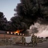 Ukrainian servicemen carry containers backdropped by a blaze at a warehouse after a bombing on the outskirts of Kyiv, Ukraine, Thursday, March 17, 2022.