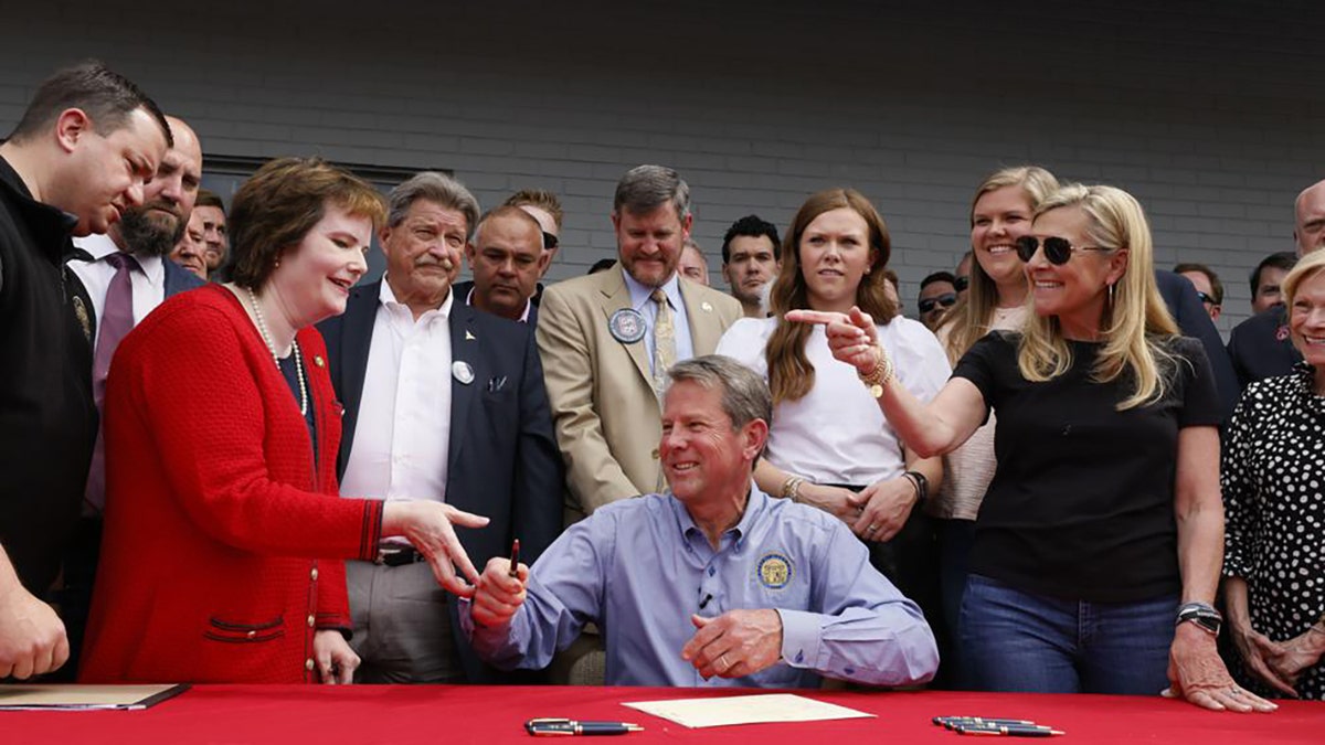 Gov. Brian Kemp hands a pen to Rep. Mandi Ballinger after he signed a bill which will allow permit less carry at a sporting goods store in Douglasville, Ga., Tuesday, April 12, 2022. (Bob Andres/Atlanta Journal-Constitution via AP)