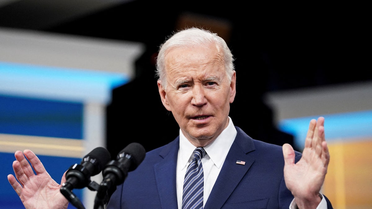 President Joe Biden speaking at podium wearing blue suit and striped tie