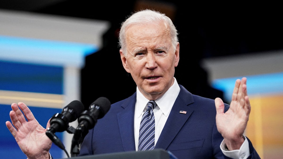 President Joe Biden speaking at podium wearing blue suit and striped tie