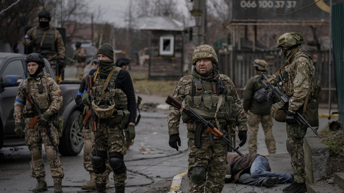 Ukrainian servicemen stand while checking bodies of civilians for booby traps, in the formerly Russian-occupied Kyiv suburb of Bucha, Ukraine, Saturday, April 2, 2022.