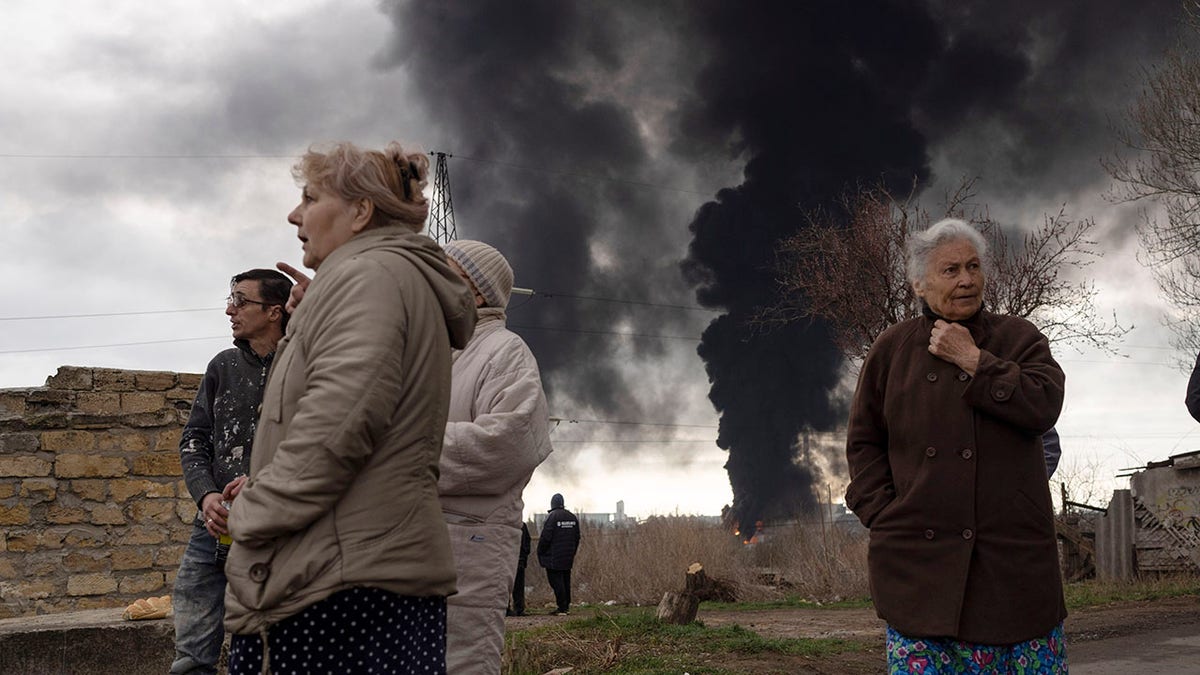 People stay in a yard as smoke rises in the air in the background after shelling in Odessa, Ukraine, Sunday, April 3, 2022. 
