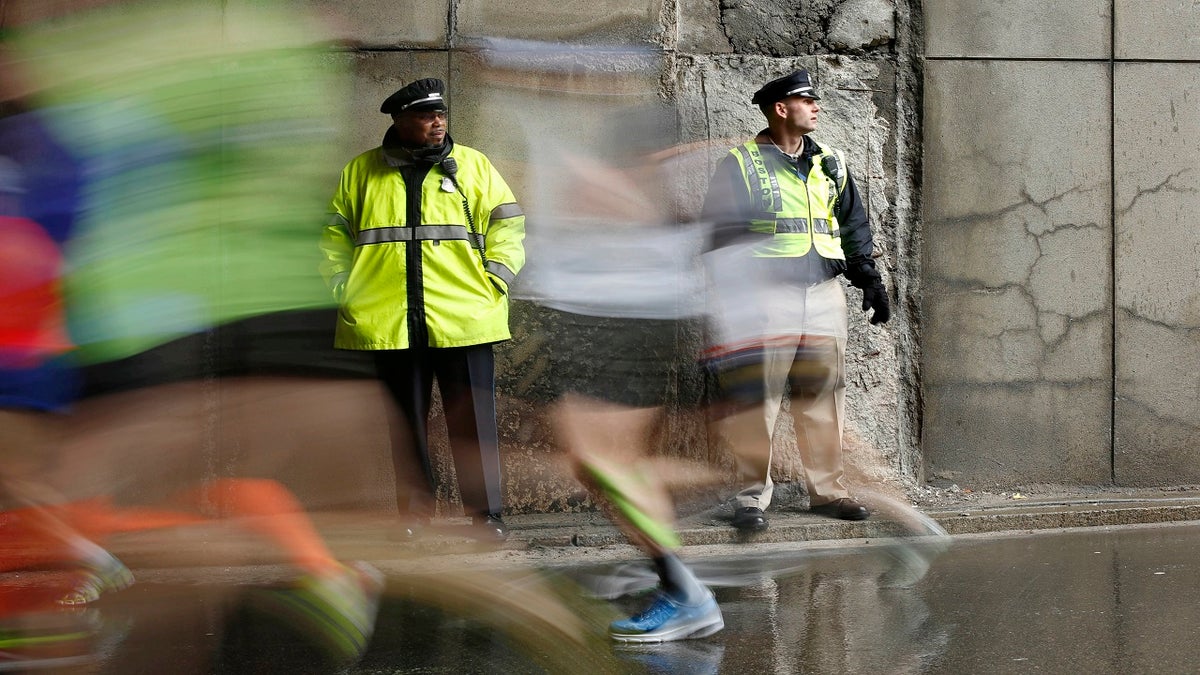 Police officers stand watch as Boston Marathon runners race