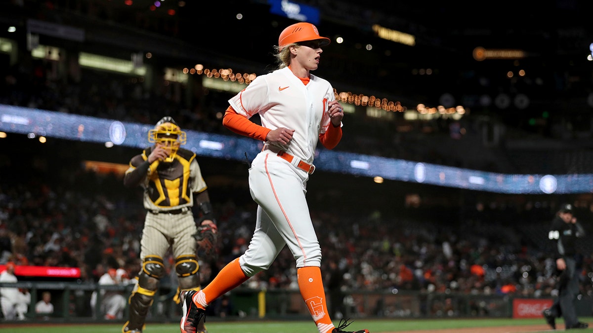 San Francisco Giants first base coach Alyssa Nakken runs to get in position, near San Diego Padres catcher Austin Nola, left, during the third inning of a baseball game in San Francisco, Tuesday, April 12, 2022.