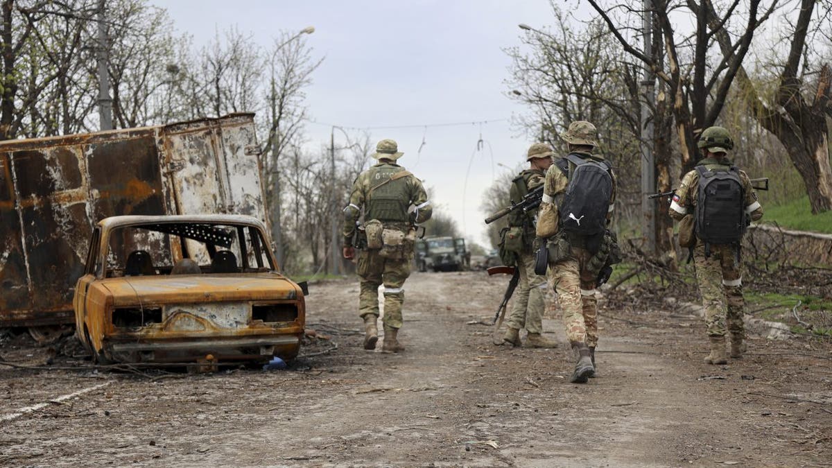 Servicemen of Donetsk People's Republic militia walk past damaged vehicles during a heavy fighting in an area controlled by Russian-backed separatist forces in Mariupol, Ukraine, Tuesday, April 19, 2022. Taking Mariupol would deprive Ukraine of a vital port and complete a land bridge between Russia and the Crimean Peninsula, seized from Ukraine from 2014.