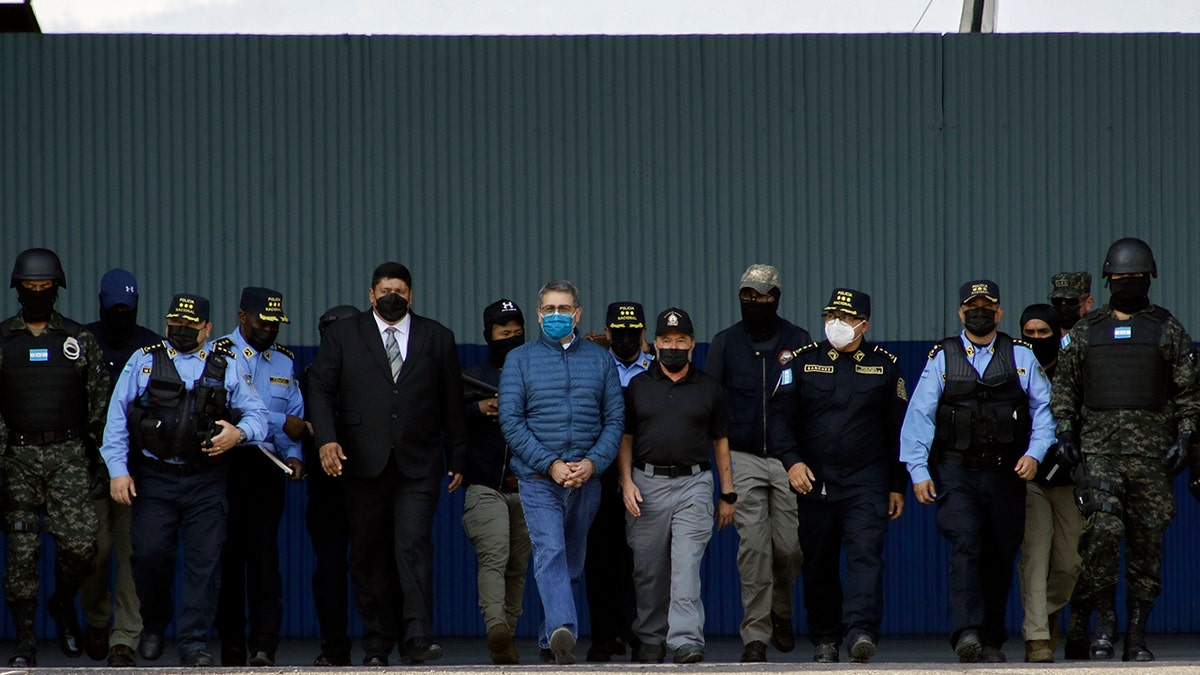 Former Honduran President Juan Orlando Hernandez, center, wearing a blue protective face mask and handcuffed, is escorted under heavy guard to a waiting aircraft at the Air Force base in Tegucigalpa, Honduras, Thursday, April 21, 2022. 