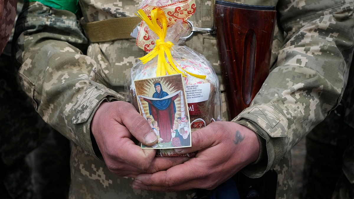 A Ukrainian soldier holds an Easter cake and an icon during a blessing ceremony on Easter eve at a military position outside Kyiv, Ukraine, Saturday, April 23, 2022. (AP Photo/Efrem Lukatsky)