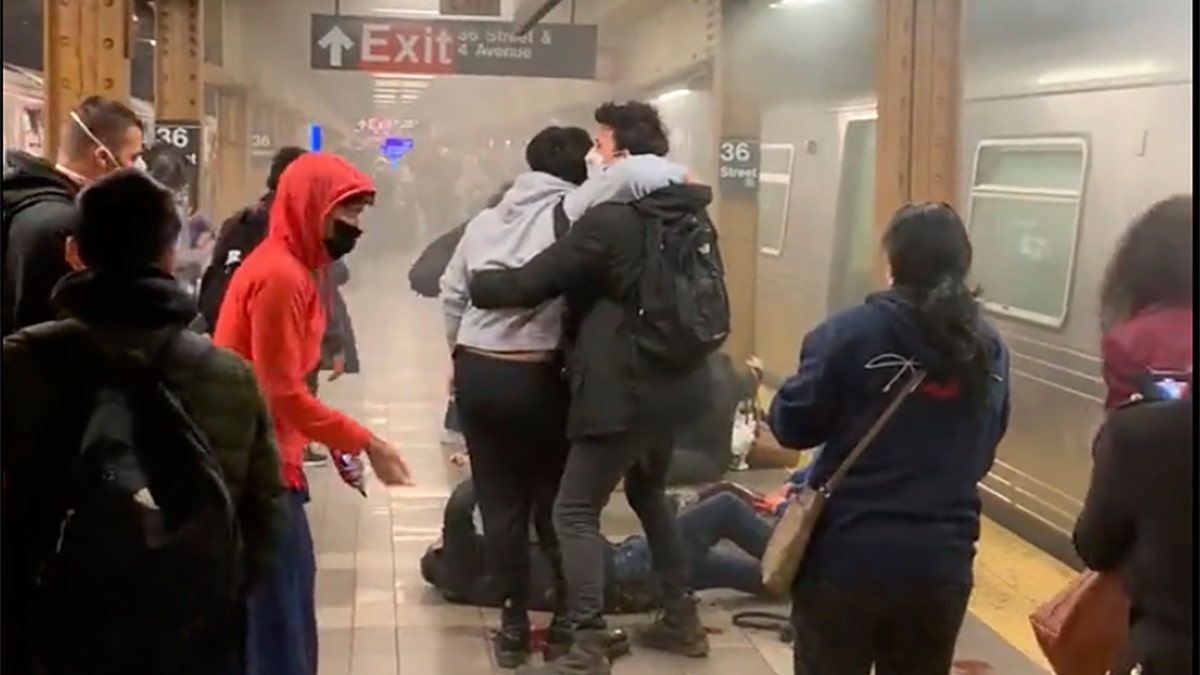 This photo provided by Will B Wylde, a person is aided outside a subway car in the Brooklyn borough of New York, Tuesday, April 12, 2022. A gunman filled a rush-hour subway train with smoke and shot multiple people Tuesday, leaving wounded commuters bleeding on a Brooklyn platform as others ran screaming, authorities said. Police were still searching for the suspect. (Will B Wylde via AP)