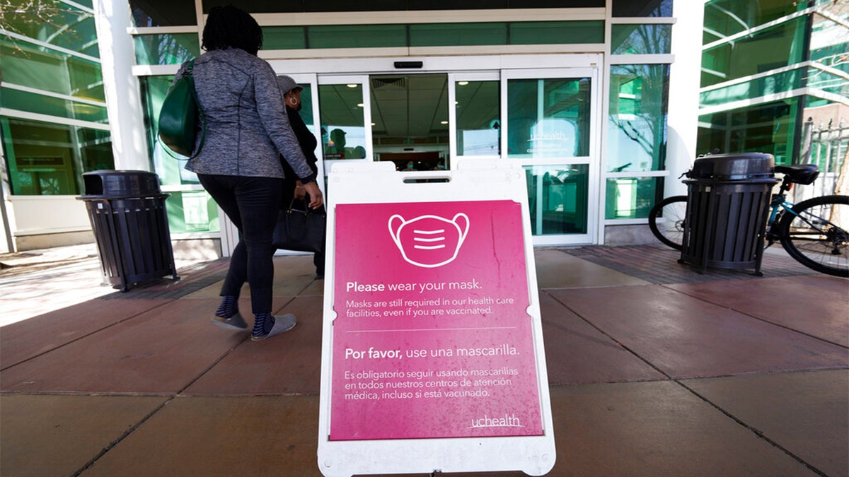 A sign advising visitors to don face coverings stands outside the main entrance to UCHealth University of Colorado hospital Friday, April 1, 2022, in Aurora, Colo. 