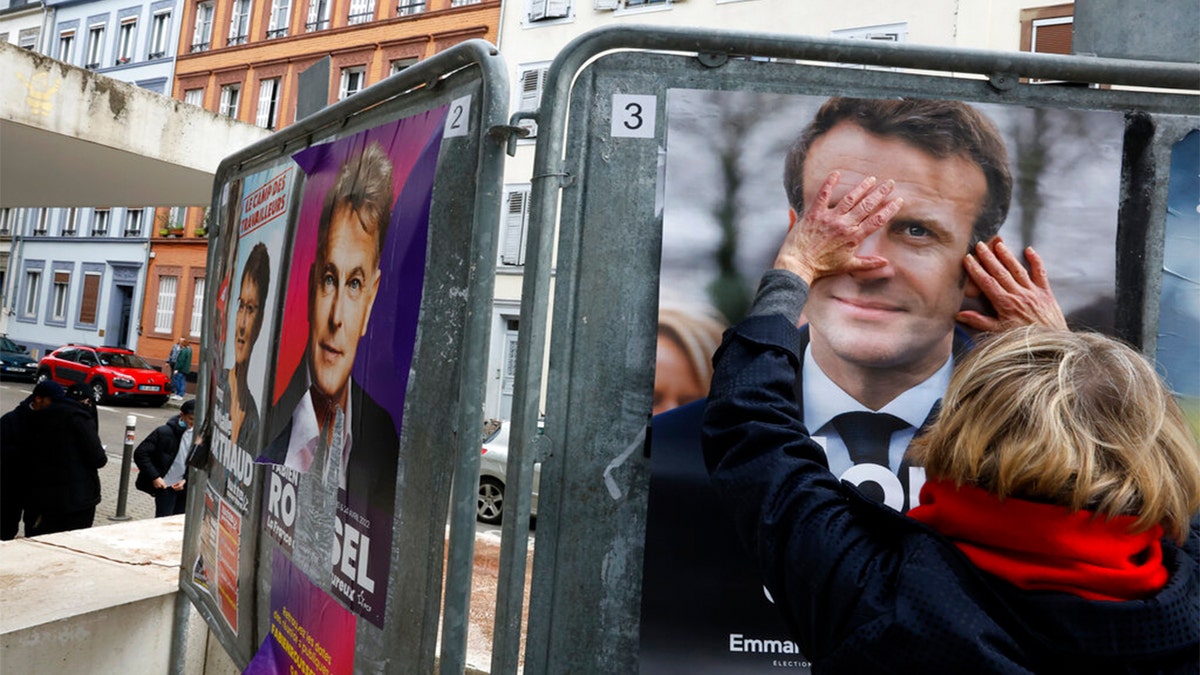 A woman touches the presidential campaign poster of French president Emmanuel Macron during the first round of the French presidential election, in Strasbourg, eastern France Sunday, April 10, 2022.