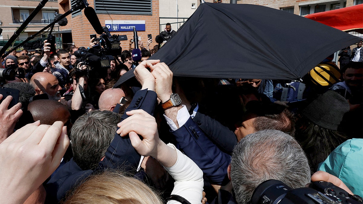 French President Emmanuel Macron is protected with an umbrella after a projectile was thrown during a walkabout at the Saint-Christophe market square in Cergy, a Paris suburb, Wednesday, April 27, 2022. (Benoit Tessier, Pool via AP)