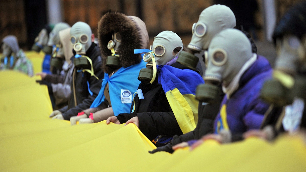 Protesters wearing gas masks hold Ukrainian national flags as they picket the Ukrainian House during a round table talks between the Ukrainian President Viktor Yanukovych, on December 13, 2013.  (Photo by Genya SAVILOV / AFP) (Photo by GENYA SAVILOV/AFP via Getty Images)