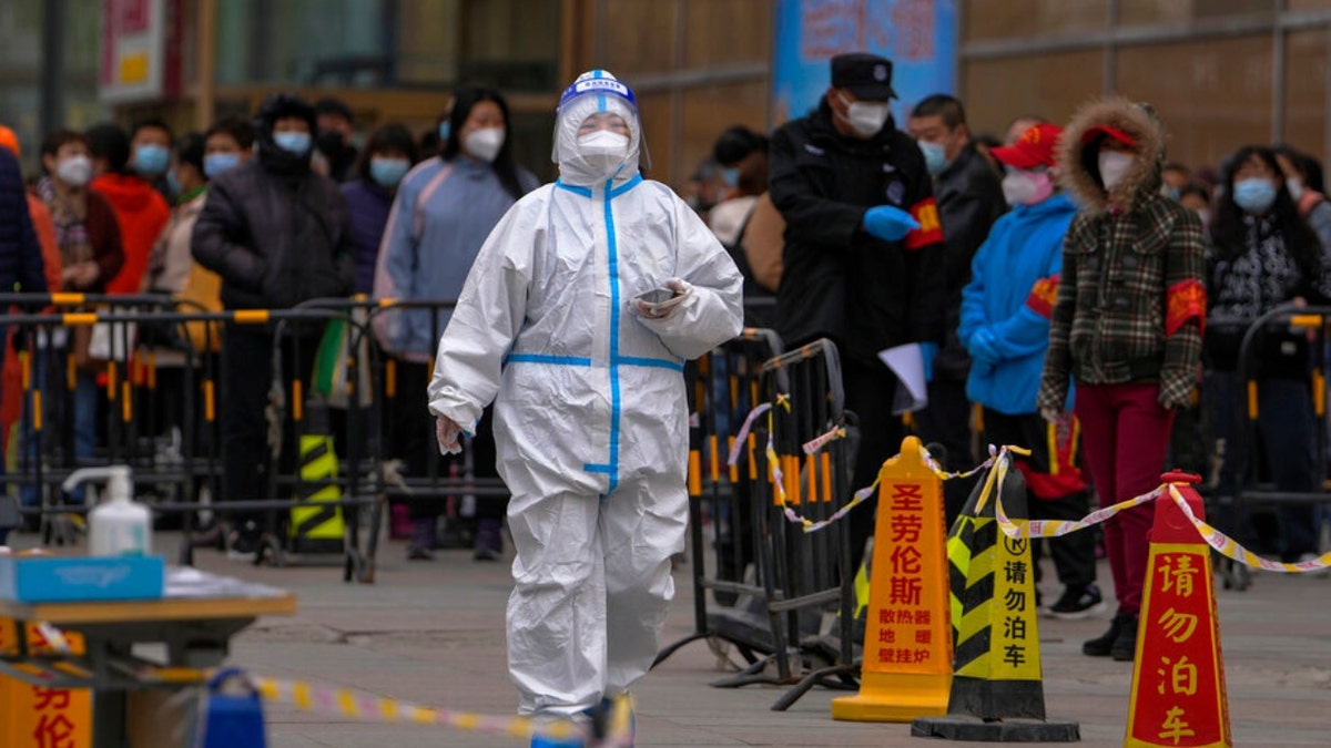A health worker walks by Beijing residents waiting for COVID-19 throat swabs