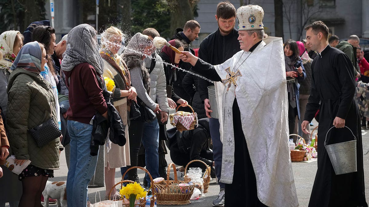 Ukrainian priest in white robes blesses and sprays holy water on congregants