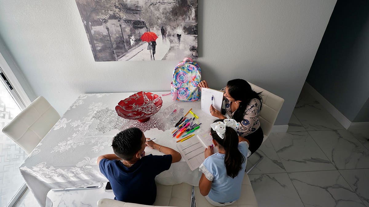 A woman helps her children with their homework at their home Tuesday, April 19, 2022, in Tampa, Florida. More immigrants from Cuba are coming to the U.S. by making their way to Mexico and crossing the border illegally. It’s a very different reality from years ago, when Cubans enjoyed special protections that other immigrants did not have. 